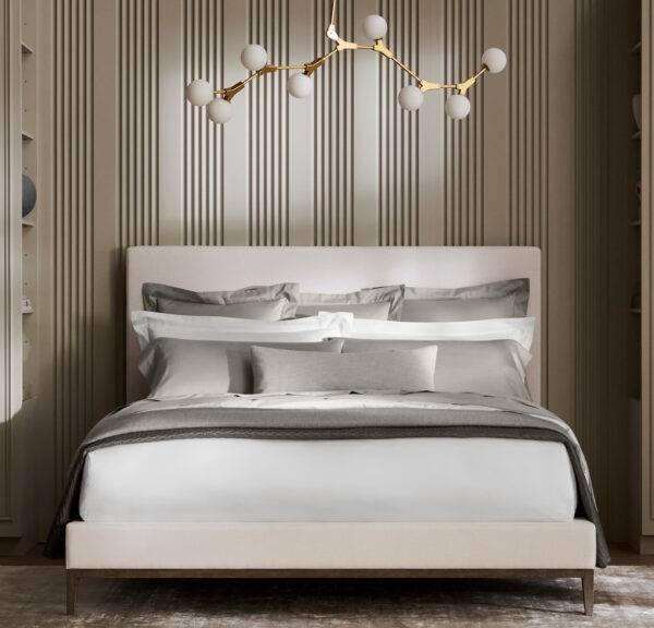 A white platform bed with crisp white sheets and duvet, accented by steel grey pillows and coverlet, sits in a modern room against a back drop of white and black striped wallpaper.