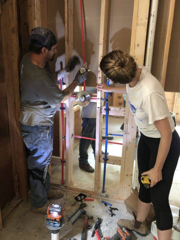 Bea looks on as plumber installs pipes in wall.
